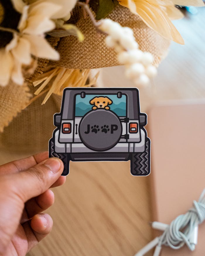 A person holding a decorative Jeep sticker featuring a cute dog illustration.